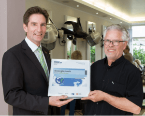 HWK-Umweltexperte Dr. Klaus Landrath (l.) überreicht das fertiggestellte Energiebuch an Friseurmeister Beatus Bußmann.